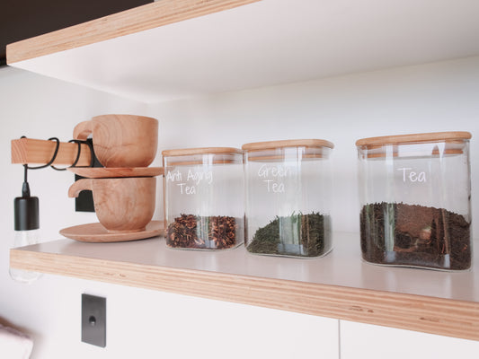 Tea-making setup with wooden cups and glass jars on a shelf.
