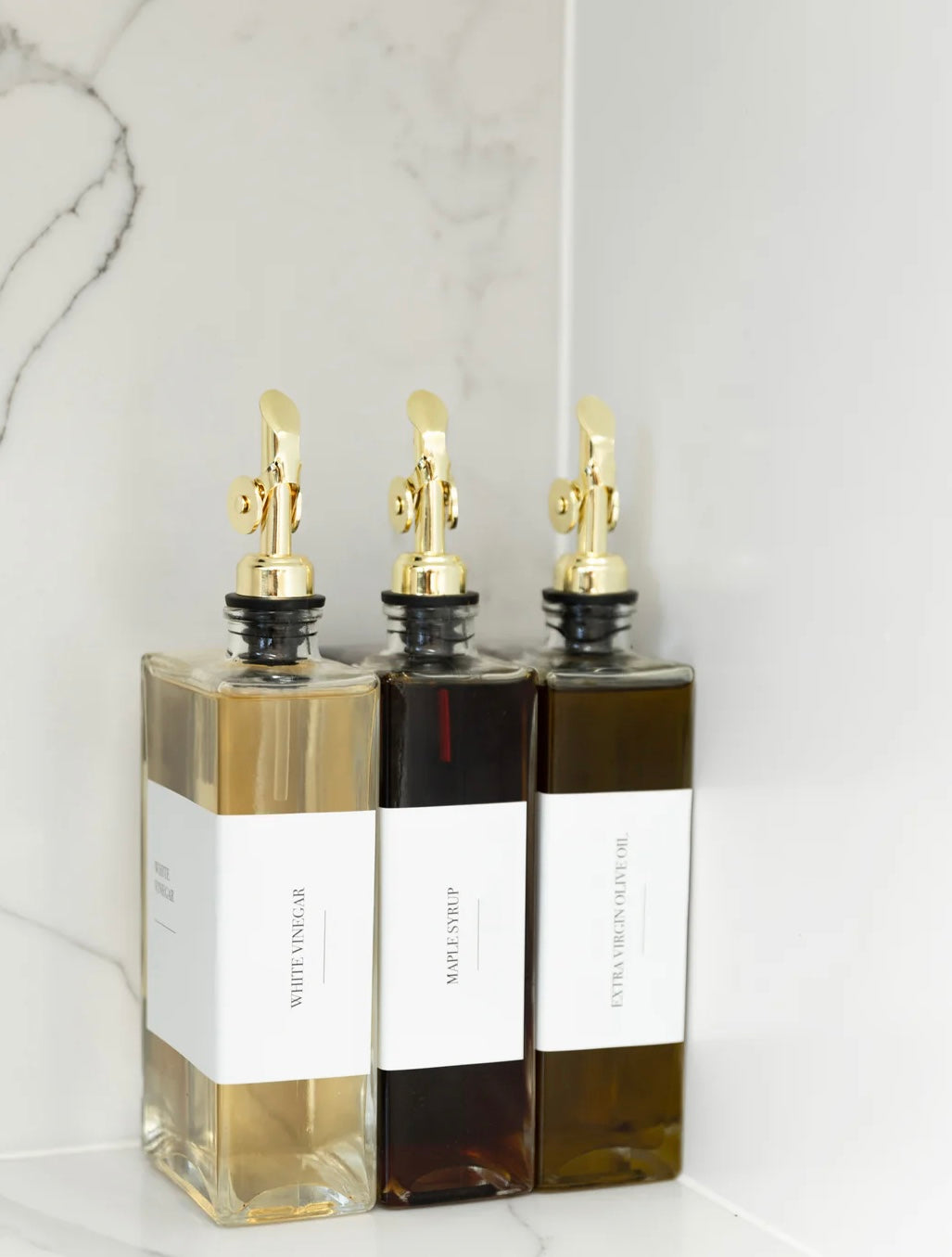 Three bottles of oil with gold nozzles on a marble surface