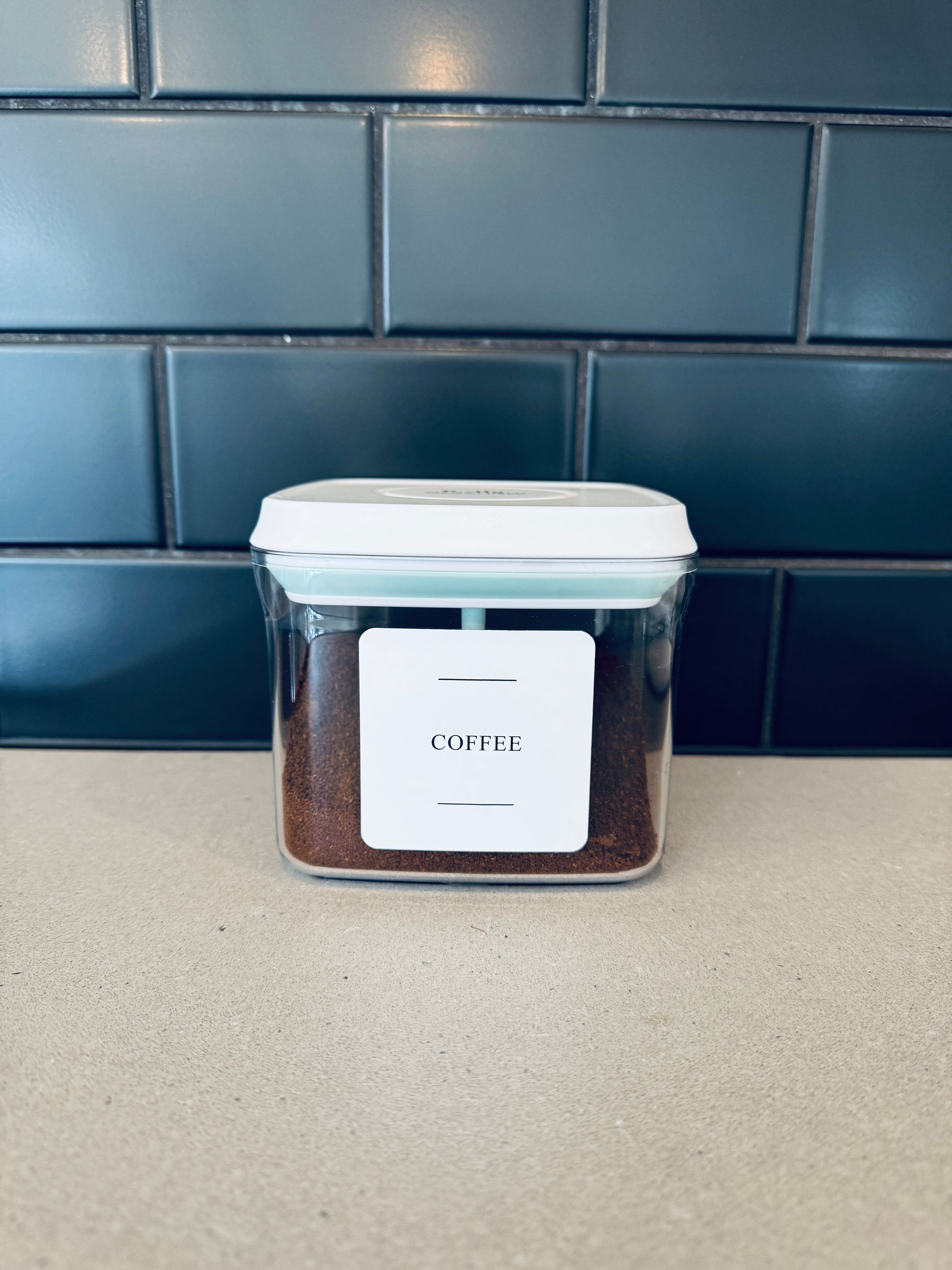 Container of coffee with a label on a countertop against a tiled wall.