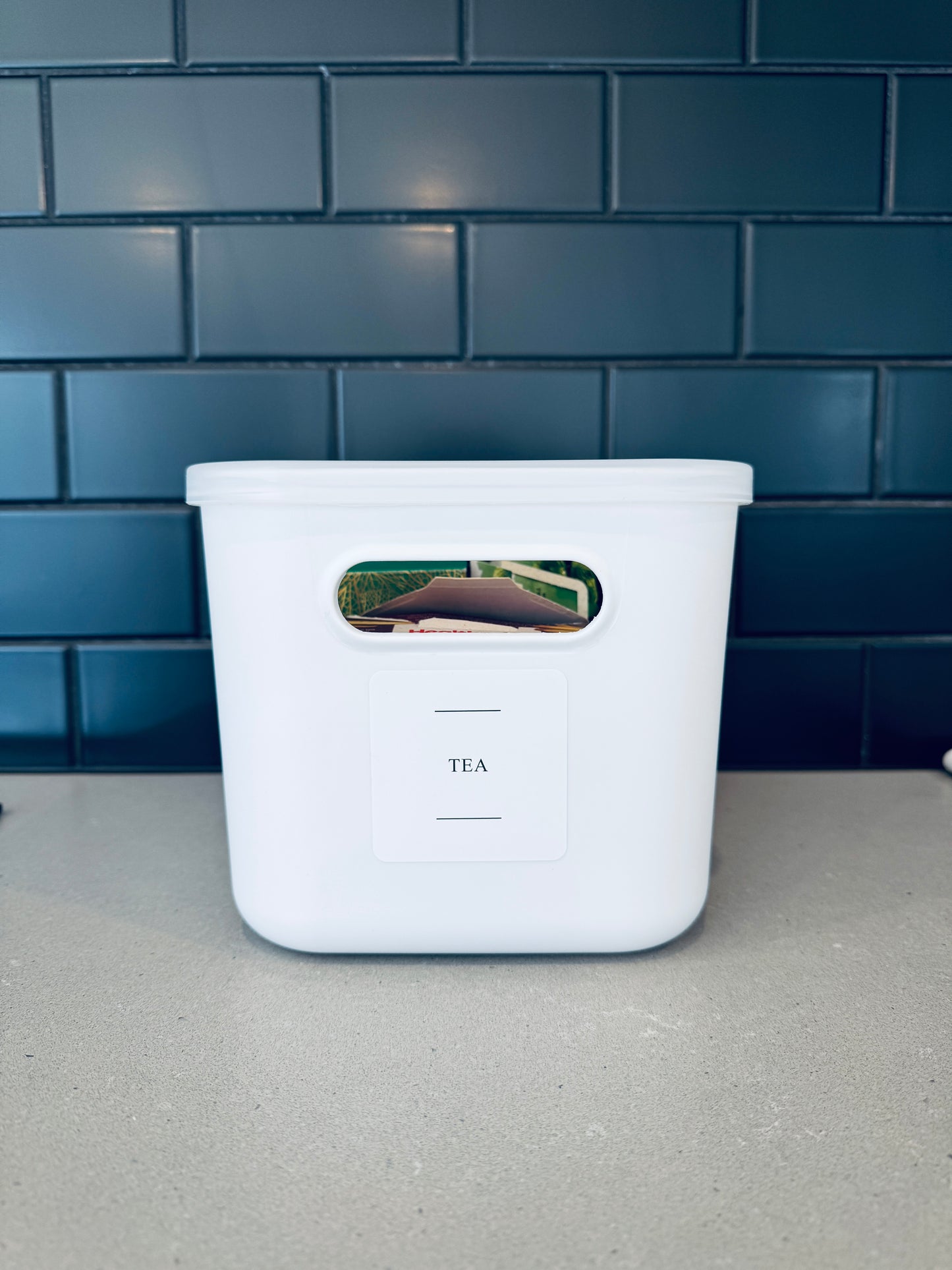 White tea storage container with a label on a gray surface and blue tiled wall background
