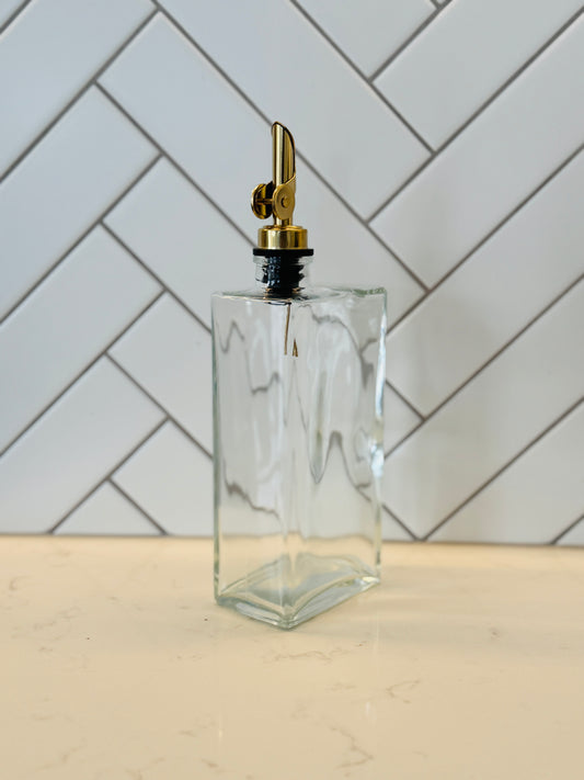 Clear glass bottle with gold cap on a light wooden surface with a white tiled wall background