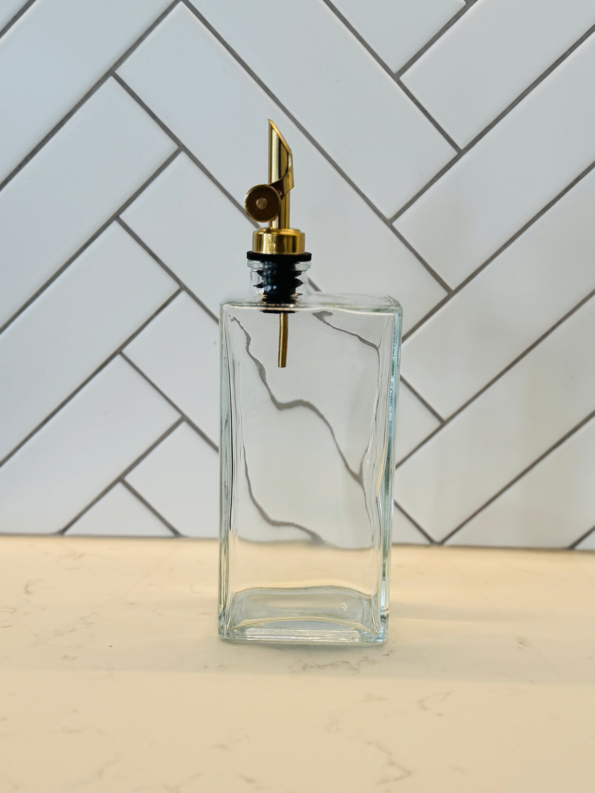 Clear glass bottle with gold cap on a light wooden surface and tiled wall background