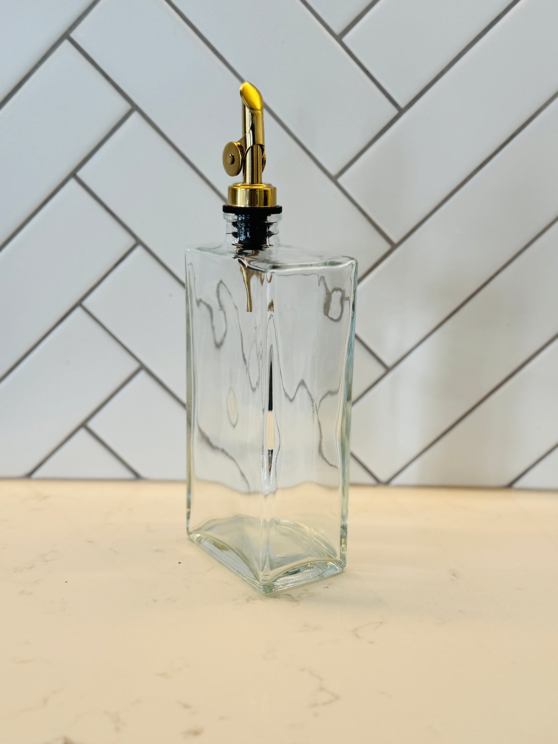 Clear glass bottle with gold cap on a light wooden surface with a white tiled wall background