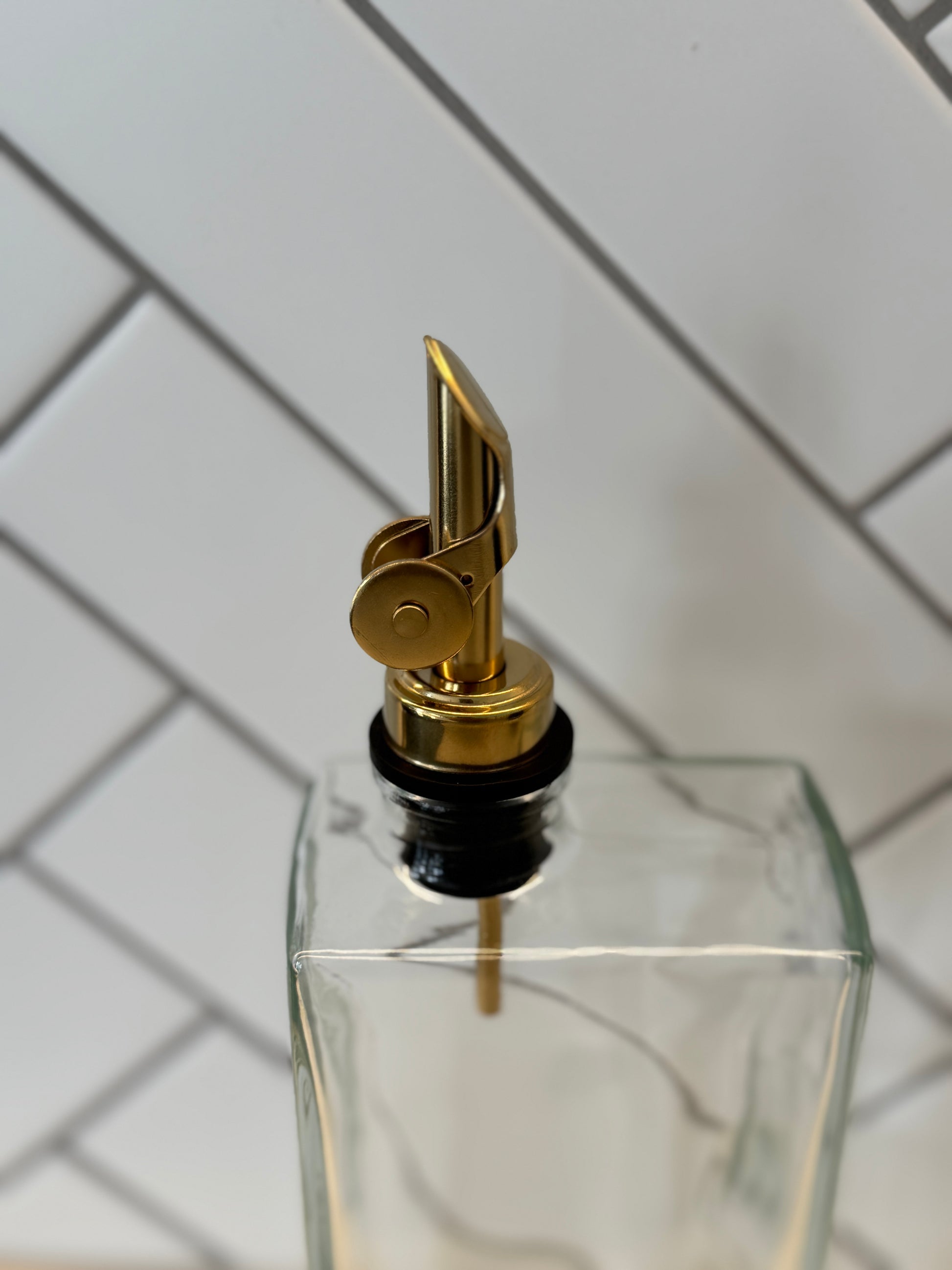 Clear glass bottle with gold nozzle on a white tiled background