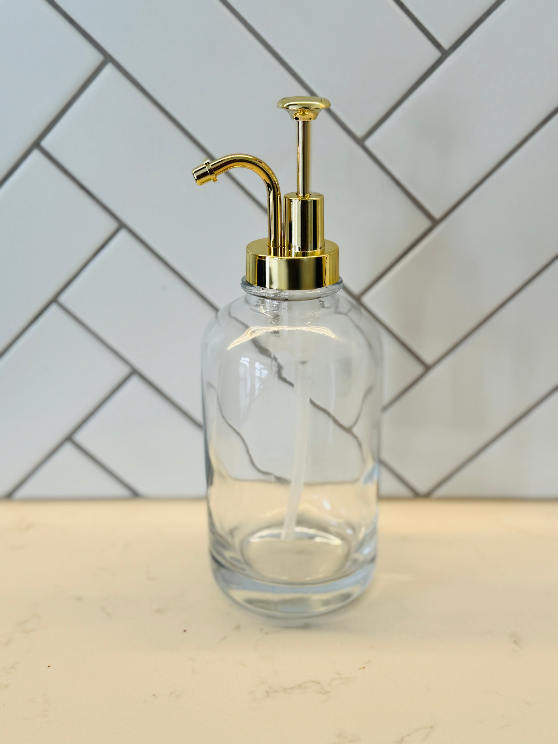 Clear glass bottle with gold pump against a tiled wall background