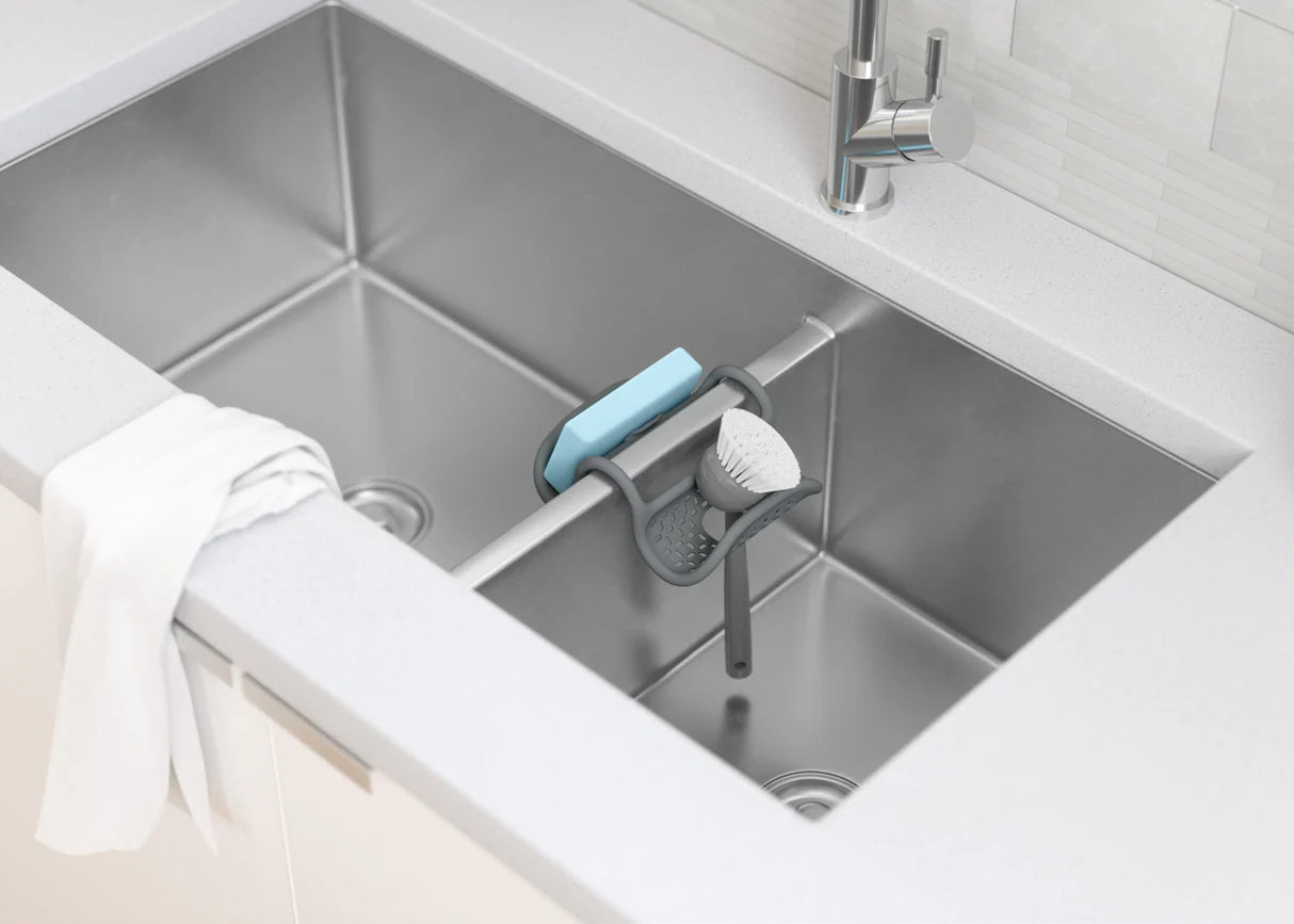 Kitchen sink with a cleaning brush and sponge holder on a white countertop.