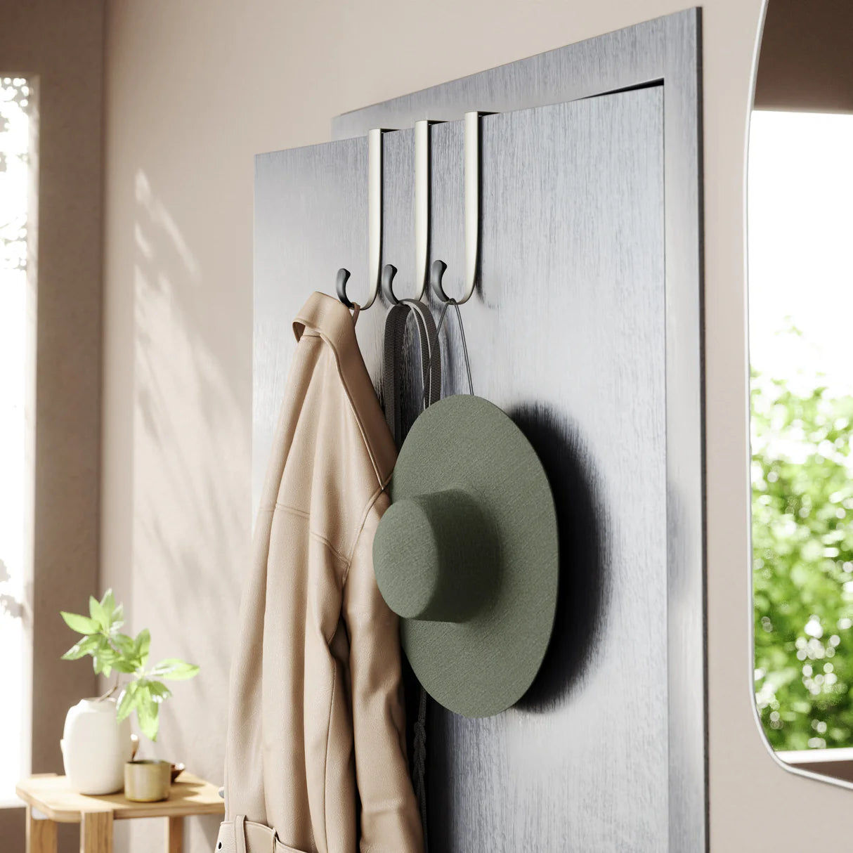 Three nickel-finish over-the-door hooks hanging on a door, holding a hat and a coat.