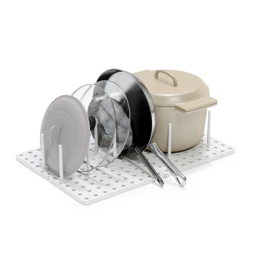 Pots, pans, and lids on a white pegboard organizer against a white background
