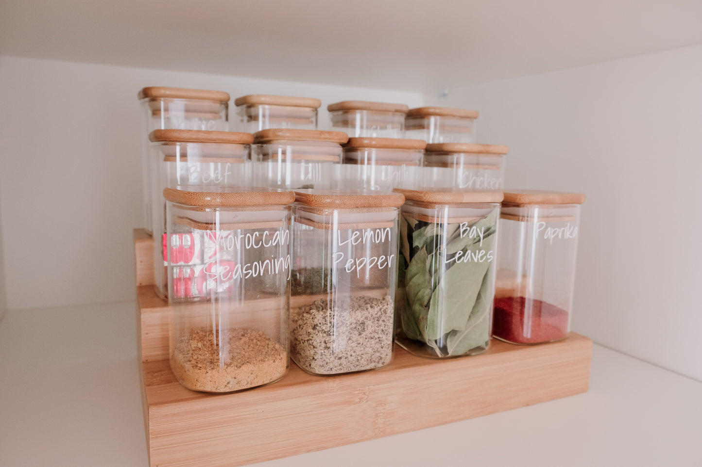 Glass square spice jars neatly arranged on bamboo rack, ideal for pantry organisation and kitchen storage NZ.