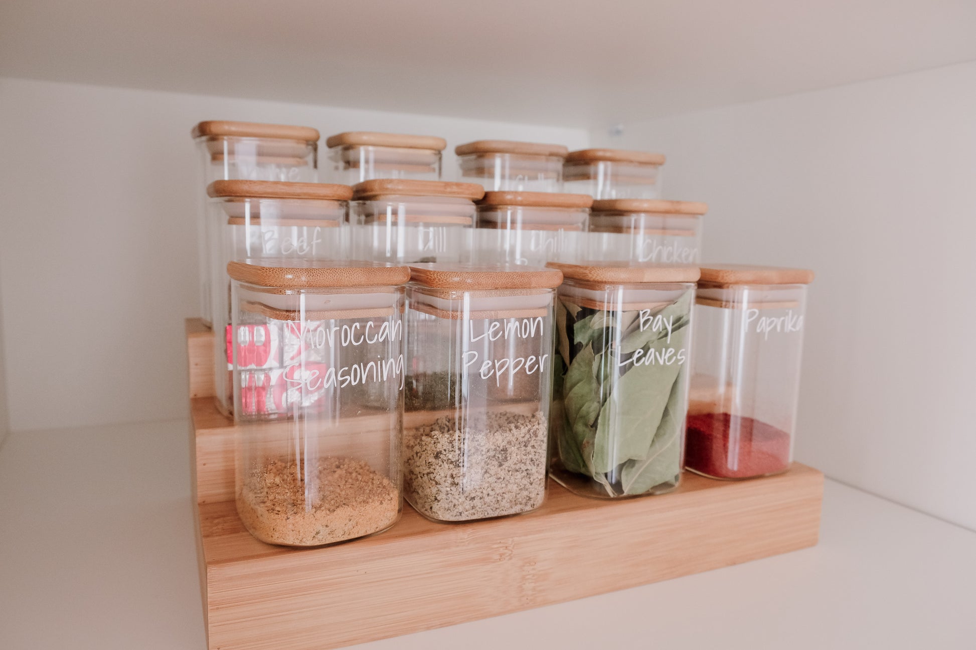 Glass square spice jars neatly arranged on bamboo rack, ideal for pantry organisation and kitchen storage NZ.