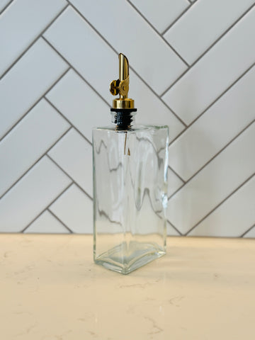 Clear glass bottle with gold cap on a light wooden surface with a white tiled wall background