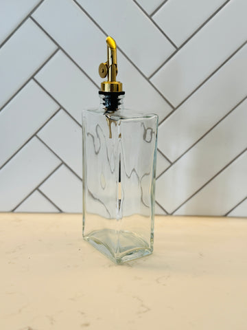 Clear glass bottle with gold cap on a light wooden surface with a white tiled wall background