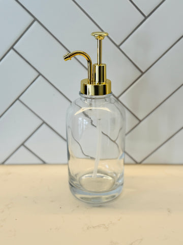 Clear glass bottle with gold pump against a tiled wall background