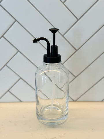 Clear glass bottle with black pump on a white countertop with a tiled wall background