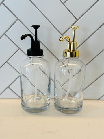 Two glass syrup dispensers with pump tops on a kitchen counter.