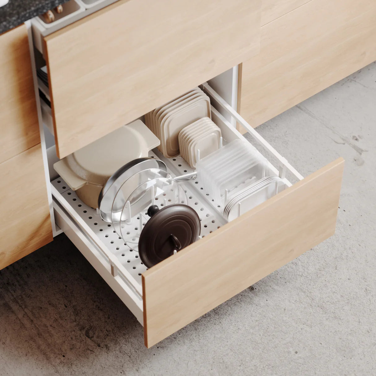 Open kitchen drawer with utensils and cookware on a light wood countertop.